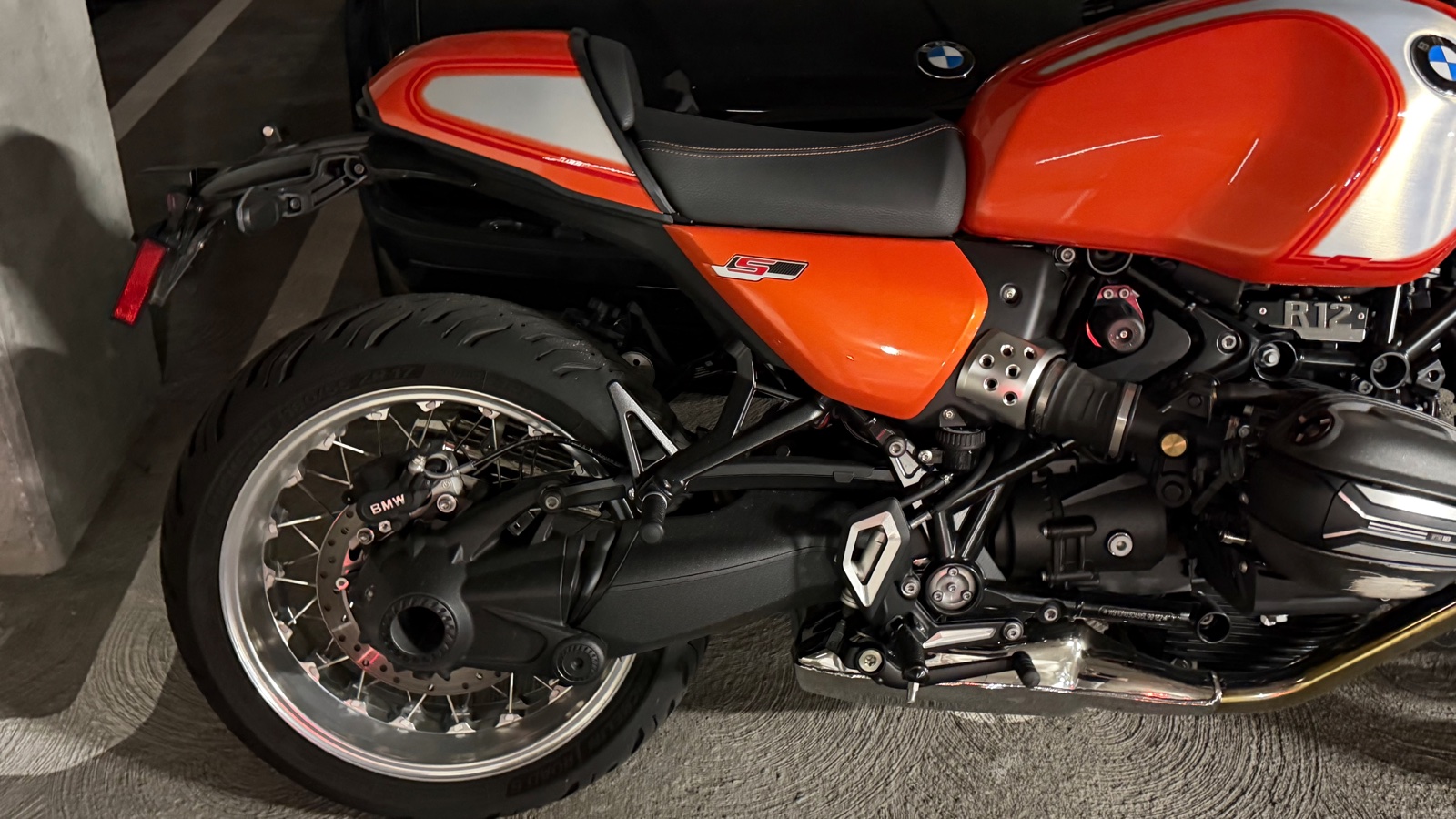 Close-up of the 2025 BMW R 12 S Lava Orange solo seat cowl, Option 719 spoked rear wheel, and Paralever shaft drive
